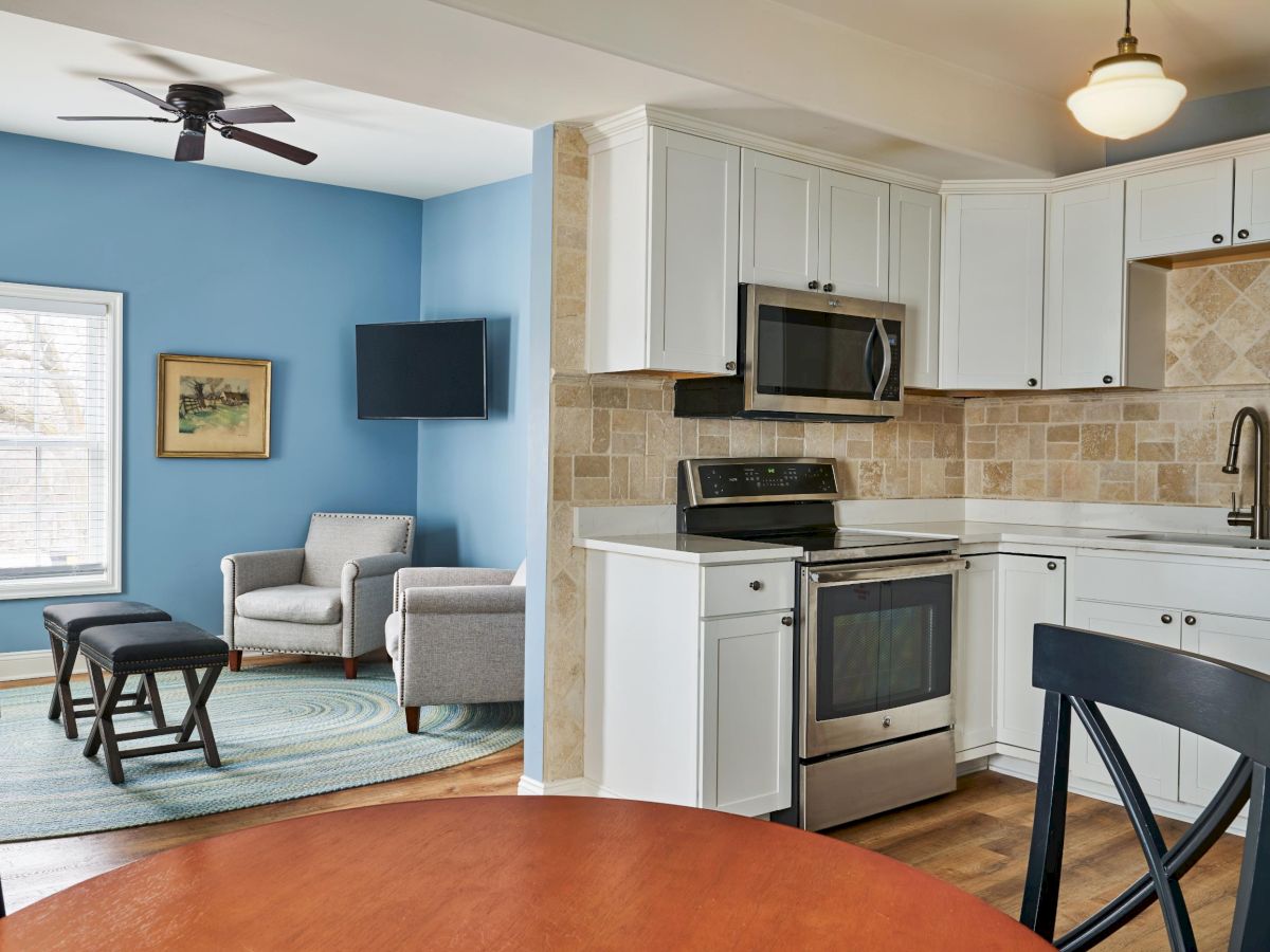 A cozy open-plan kitchen and living area with white cabinets, blue walls, and a seating area.