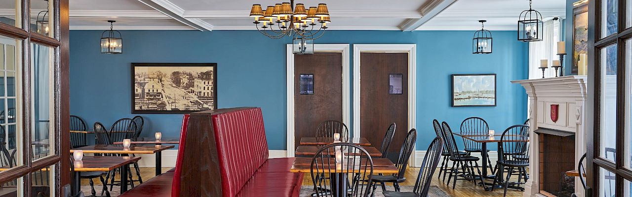 The image shows a cozy dining room with red booth seating, wooden tables, black chairs, blue walls, and framed pictures, creating a warm atmosphere.