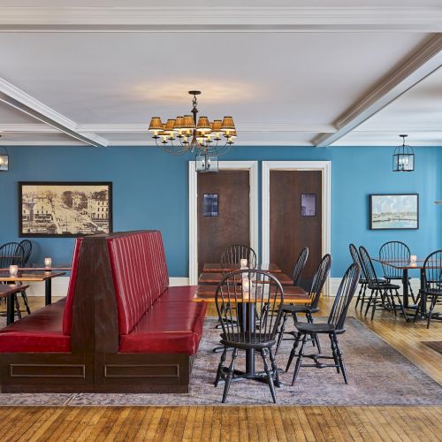 The image shows a cozy dining room with red booth seating, wooden tables, black chairs, blue walls, and framed pictures, creating a warm atmosphere.