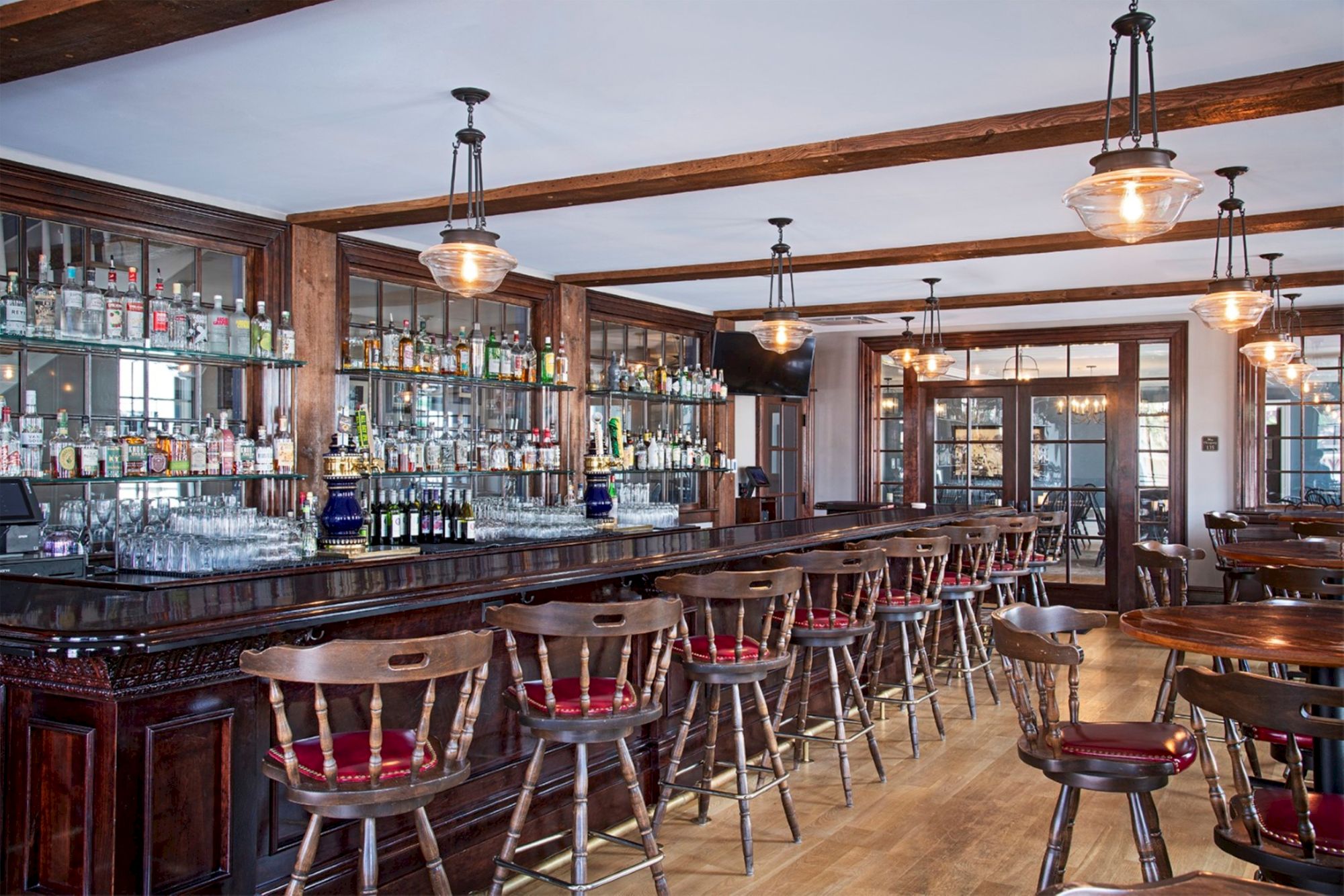 A cozy bar with wooden furnishings, lined with stools, and a wide selection of drinks on shelves behind the counter, with warm lighting.